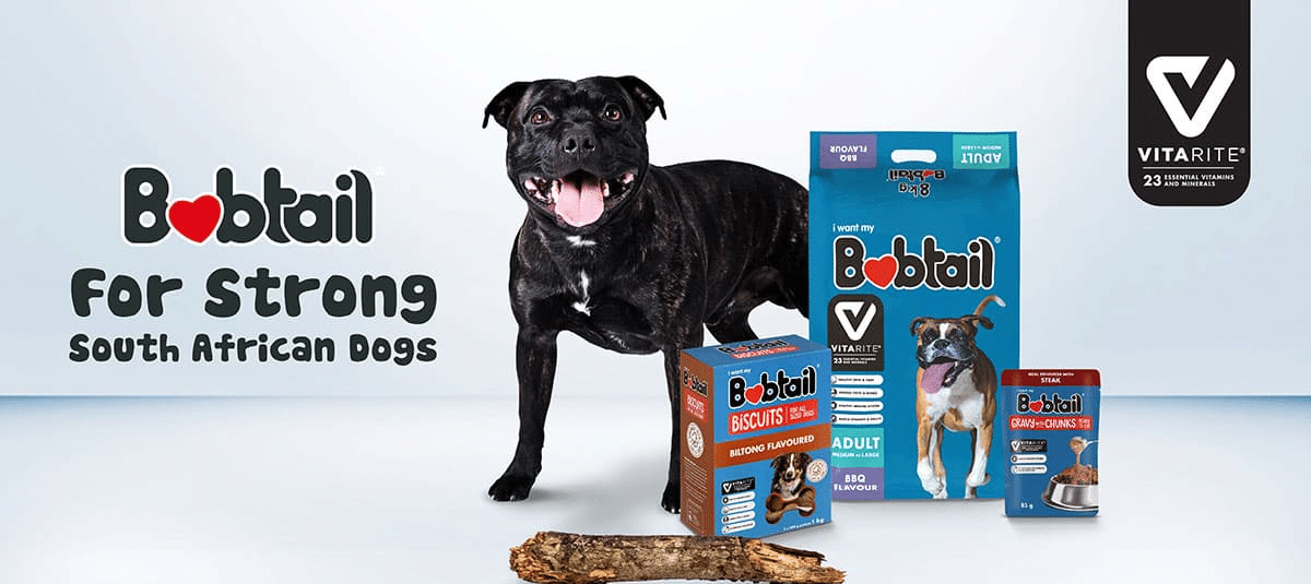 A happy black dog stands beside Bobtail dog food products, including dry food and treats, with the text Bobtail for Strong South African Dogs and the Vitarite logo in the background.