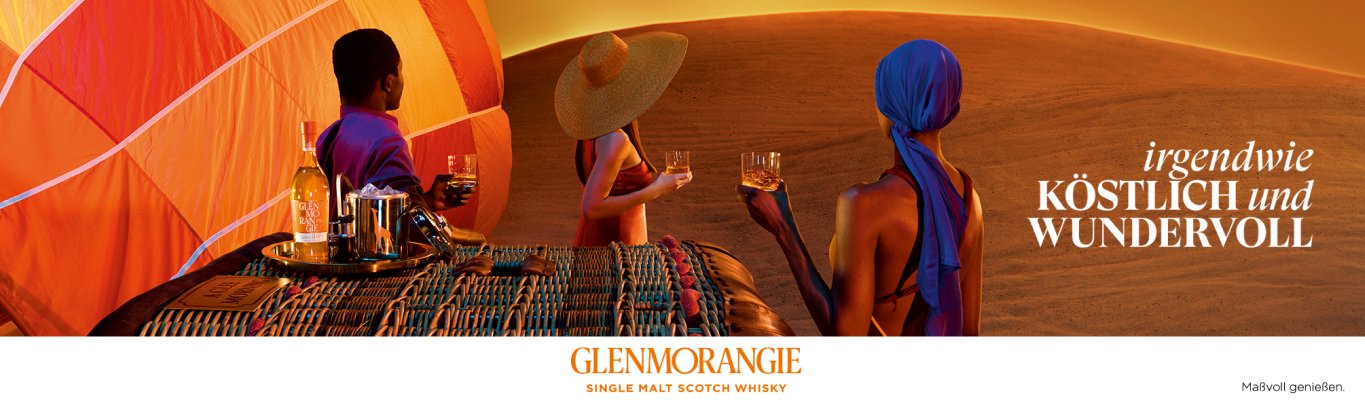 Three people in colorful clothing enjoy whisky near a table set with bottles and glasses in a desert with orange sand dunes. The text reads, irgendwie KÖSTLICH und WUNDERVOLL. Glenmorangie branding is visible below.