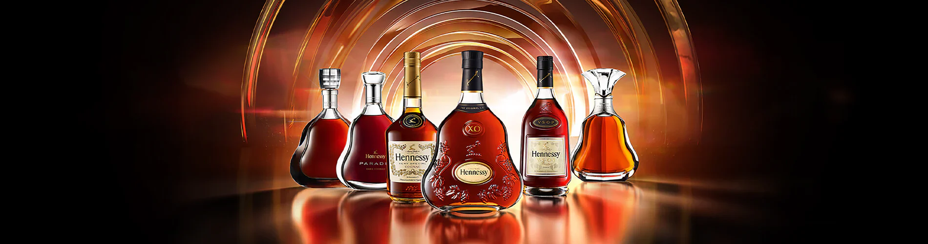 Six bottles of Hennessy cognac, each with unique shapes and labels, are displayed in a row against a dark, glowing background with golden arcs, creating a luxurious and elegant setting.
