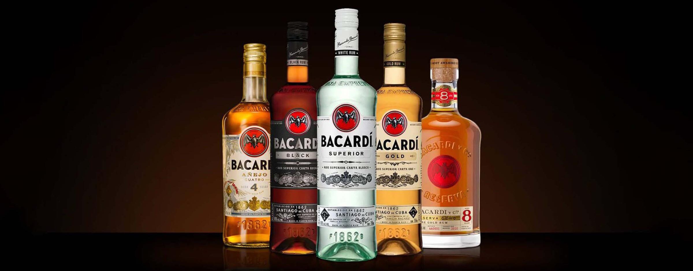 Five Bacardí rum bottles are displayed in a row against a dark background, featuring different varieties and label colors, including gold, white, and dark rum selections.